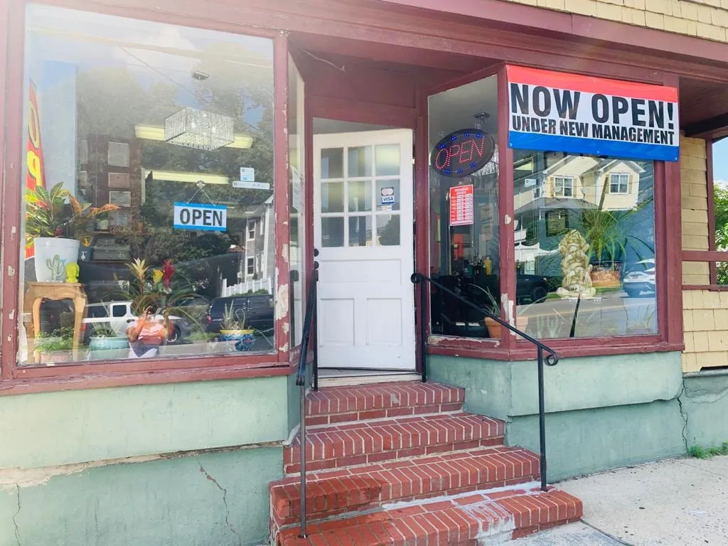 The storefront at 114 North Broad Street: display windows in dark red frames, a white door, red-brick steps and a "Now open, under new management" banner