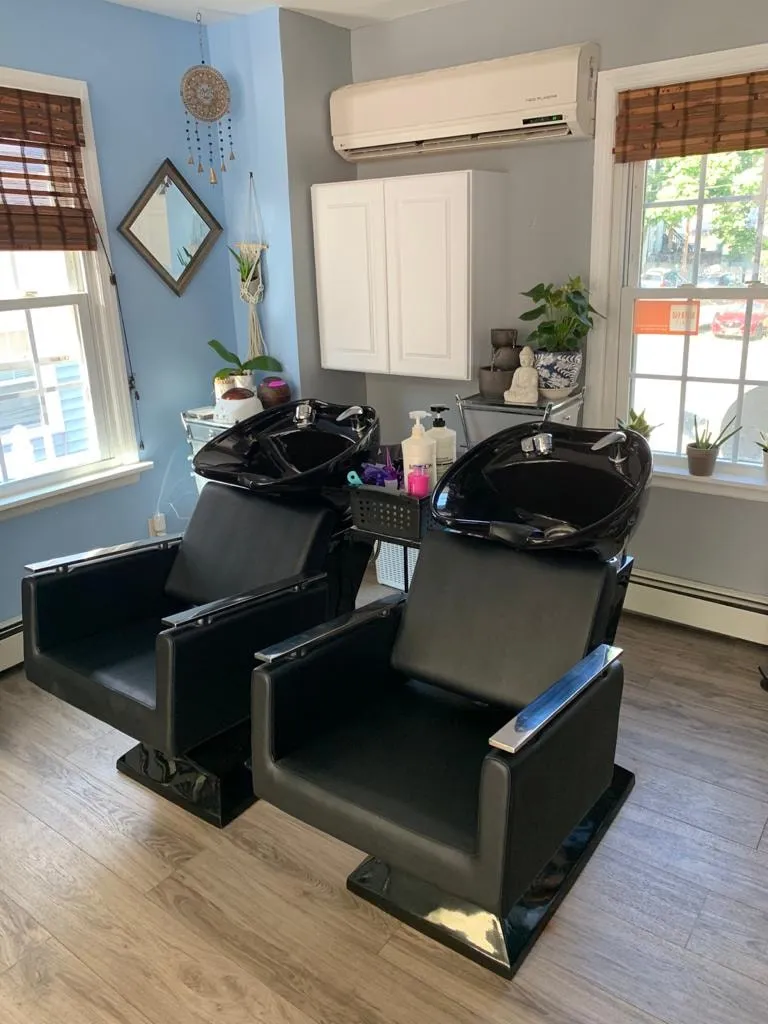 Two black shampoo chairs under a window in the sky-blue shampoo area