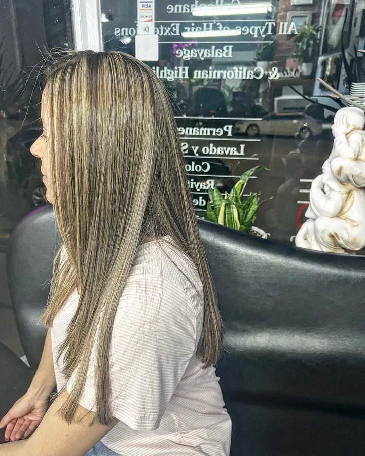 Straight brown hair with fine blonde highlights, in front of the salon window lettered with its services